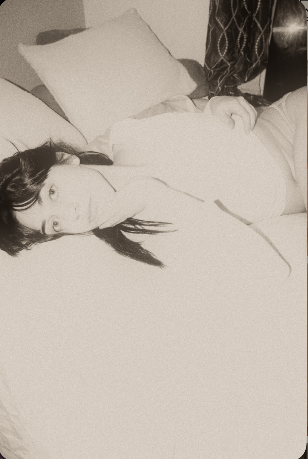 Tori May resting on a bed in soft window light, black and white film photograph